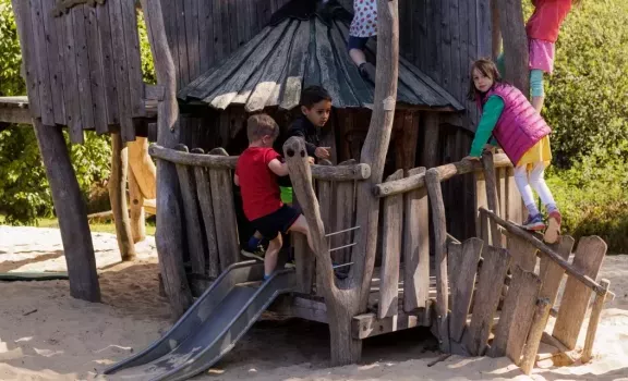 Kinder spielen auf dem Spielplatz der Kita und Klettern auf einem Holzturm.