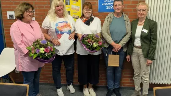 Fünf Frauen stehen vor einer Backsteinwand. Drei von ihnen haben ein Geschenk in der Hand.