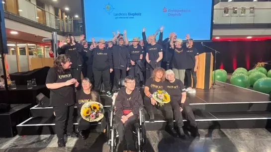 Die Trommelgruppe Unikat ist auf einer Bühne im Hintergrund ist eine Leinwand auf der