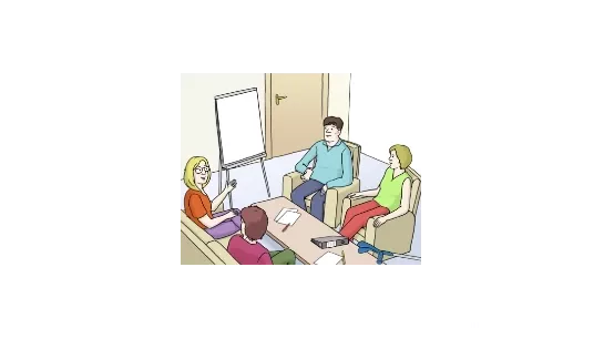 Vier Mitarbeiter sitzen um einen Tisch, sprechen miteinander. Dahinter steht ein leeres Flipchart.