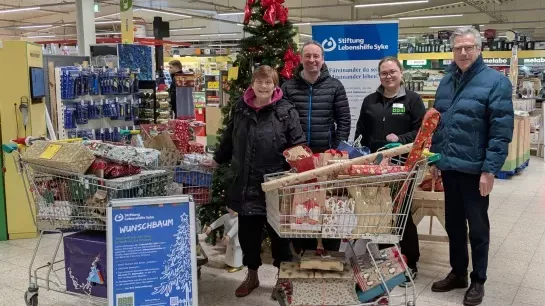 Wunschbaum-Aktion Zwei Frauen und zwei Männer stehen vor einem Weihnachtsbaum. Daneben stehen drei Einkaufswagen voll mit Geschenken.
