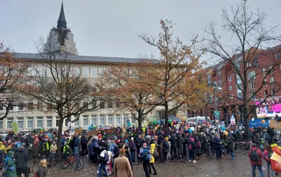 Viele Menschen stehen auf einem großen Platz. Sie halten Luftballons und Plakate in der Hand.