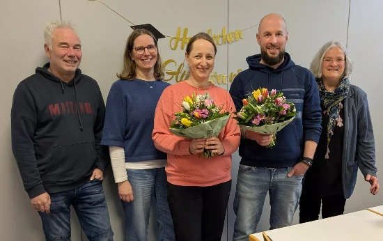 In der Mitte stehen ein Mann und eine Frau mit einem Blumenstrauß. Rechts und links davon stehen noch zwei Frauen und zwei Männer. Alle lächeln.