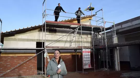 Richtfest beim Anbau der Kita Tausendschön Nina Becker steht vor dem Anbau, auf dem Gerüst stehen zwei Dachdecker, dahinter ist der Richtkranz zu sehen.